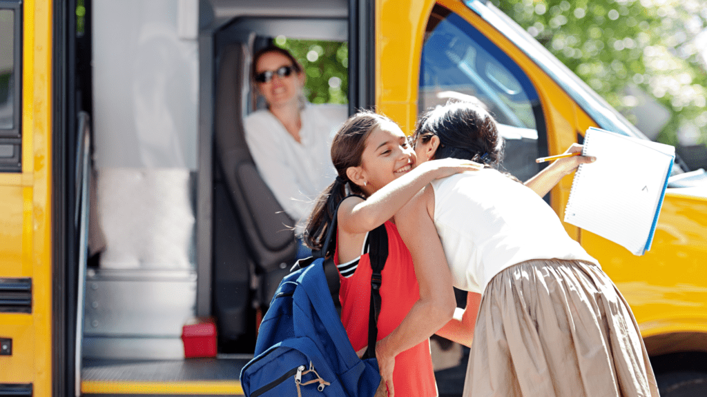 a mother hugging her daughter in front of a school bus