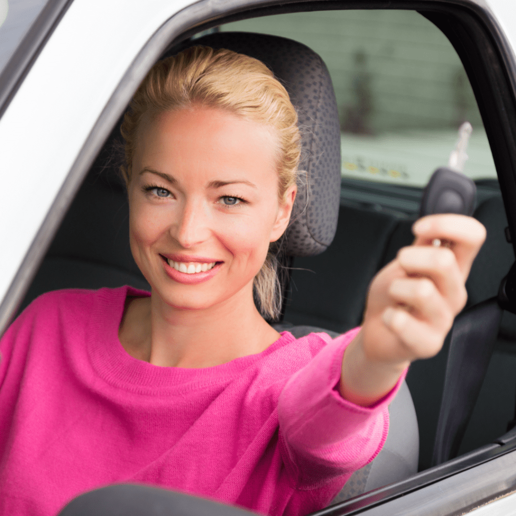 person in a car rental smiling and holding up the key to the car