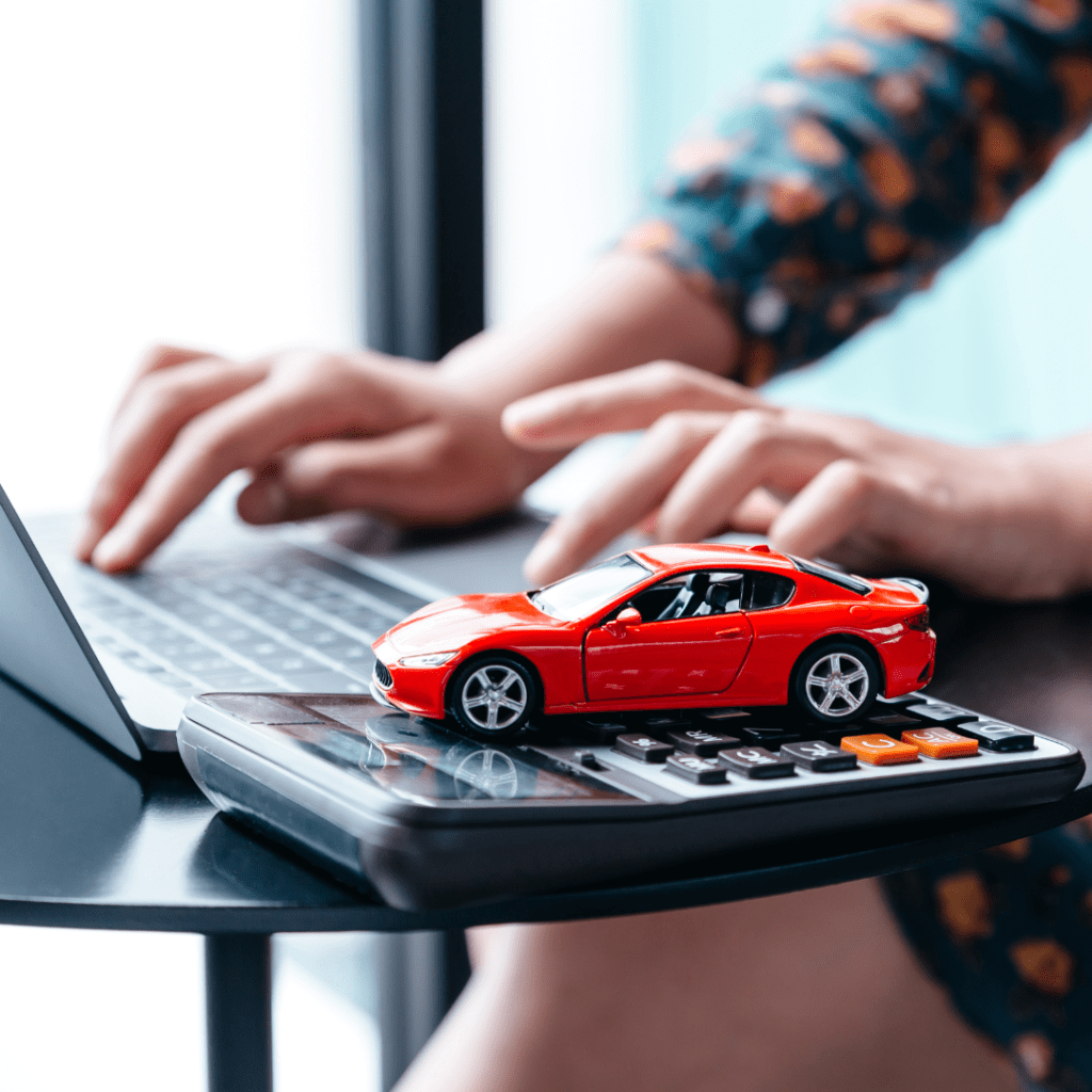 person on a laptop next to a toy car on a calculator representing how to save money on a car rental