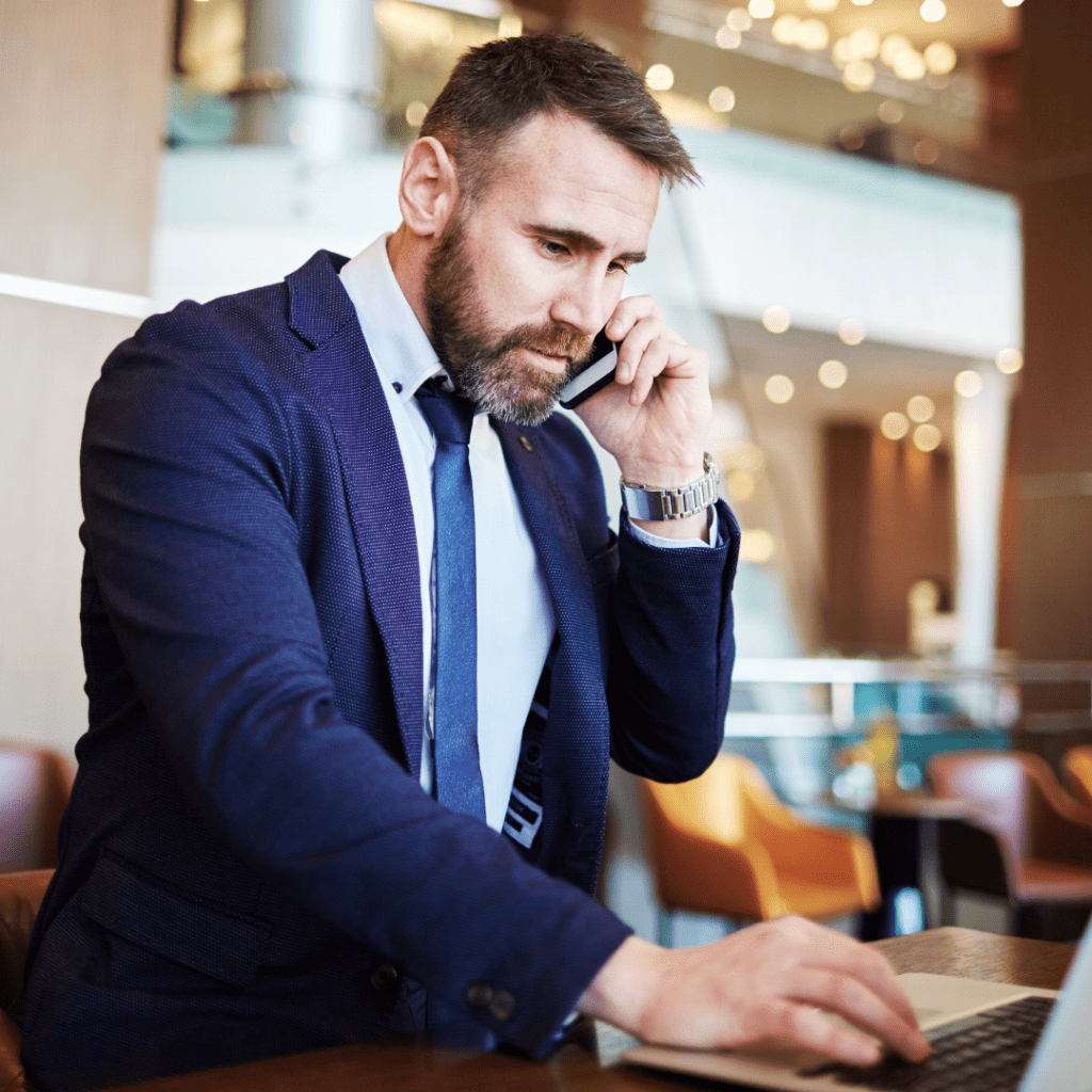 a business person on the phone and a laptop representing Rental Cars vs. Ride Shares For Business Travel