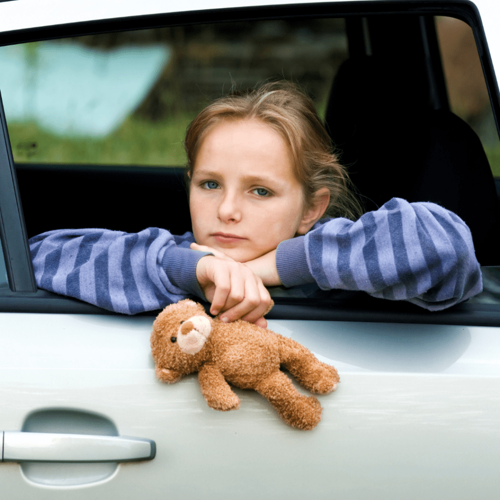 Sad child with a teddy bear looking out of the back window of a car showing they're having a bad car rental experience